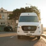 White 20 seat party limo in Sydney, a Mercedes Sprinter photographed front-on in golden hour light with the black party limo parked behind