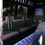 Interior of a black 20 seat party limo in Sydney showing diamond-stitched leather bench seating, blue overhead mood lighting and the LED floor viewed from the entry door