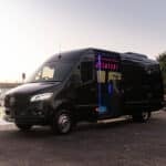 Black 20 seat party limo in Sydney, a Mercedes Sprinter parked by the water at dusk with the side door open showing pink and blue LED interior lighting