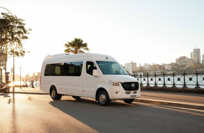 White 20 seat party limo in Sydney, a Mercedes Sprinter parked by the harbour at golden hour with the city skyline in the background
