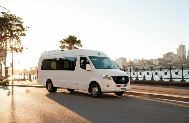 White 20 seat party limo in Sydney, a Mercedes Sprinter parked by the harbour at golden hour with the city skyline in the background