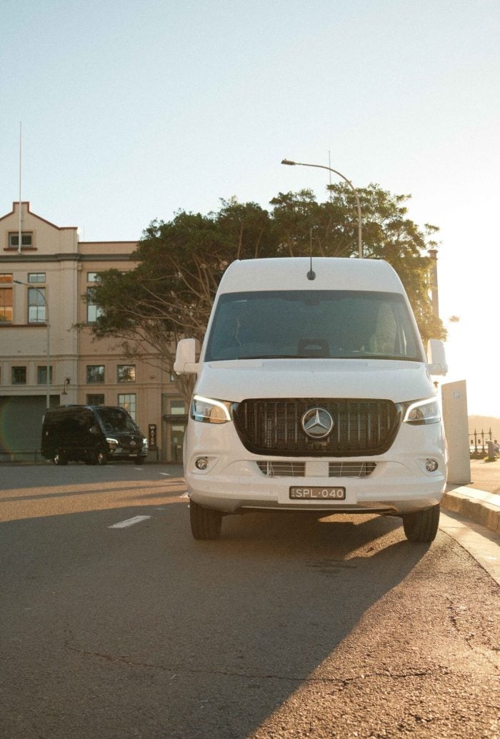 White 20 seat party limo in Sydney, a Mercedes Sprinter photographed front-on in golden hour light with the black party limo parked behind