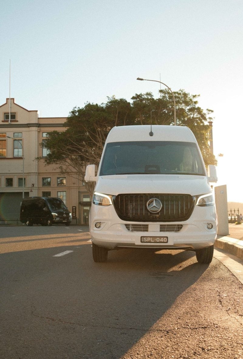 White 20 seat party limo in Sydney, a Mercedes Sprinter photographed front-on in golden hour light with the black party limo parked behind