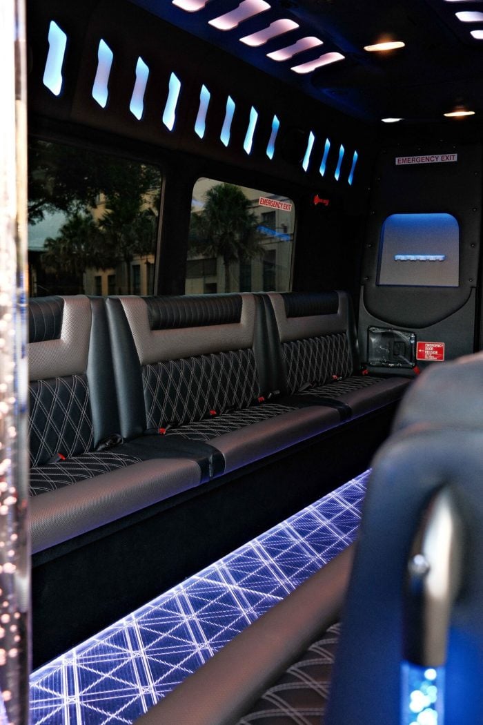 Interior of a black 20 seat party limo in Sydney showing diamond-stitched leather bench seating, blue overhead mood lighting and the LED floor viewed from the entry door