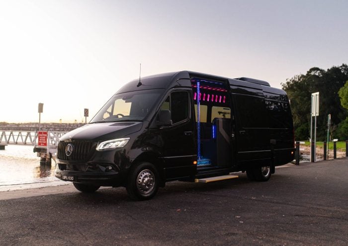 Black 20 seat party limo in Sydney, a Mercedes Sprinter parked by the water at dusk with the side door open showing pink and blue LED interior lighting